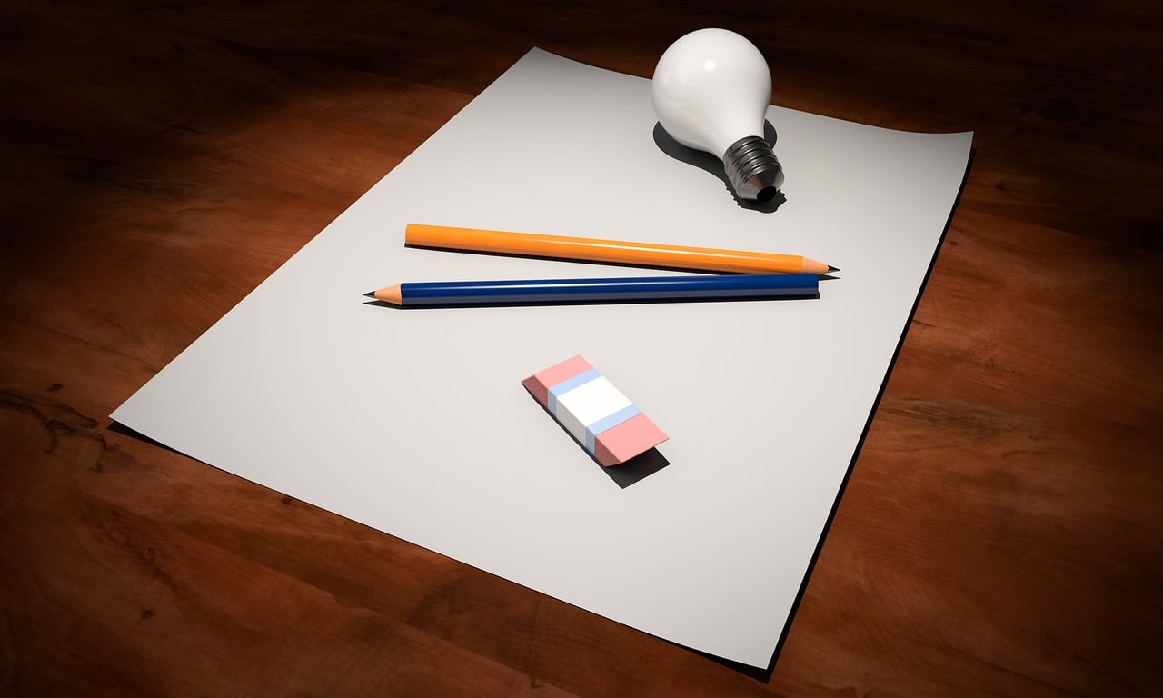 Two pencils, an eraser, and lightbulb sit on top of a piece of blank paper