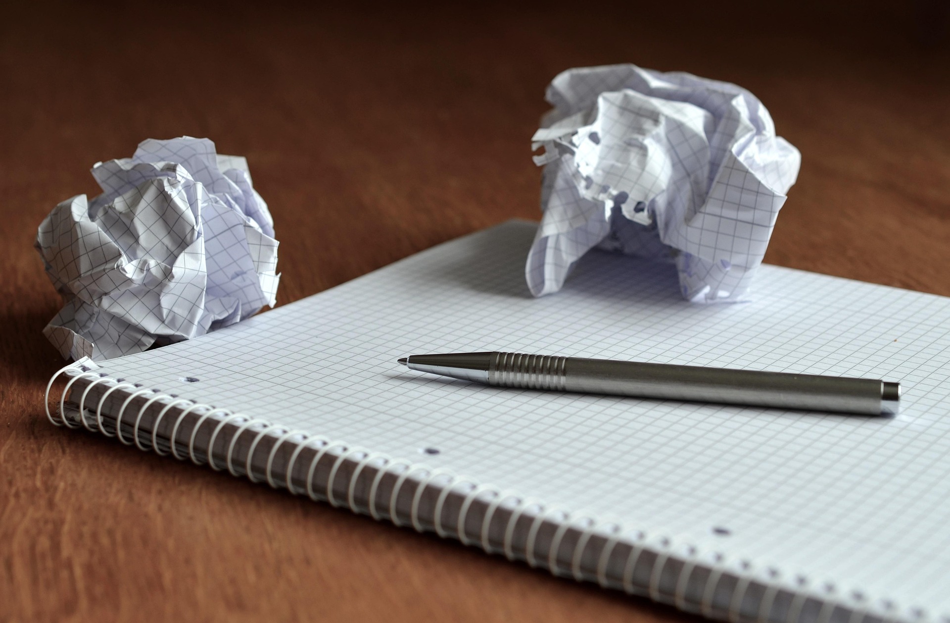 A pen lies on a gridded paper notebook with two crumpled balls of paper sitting to the side